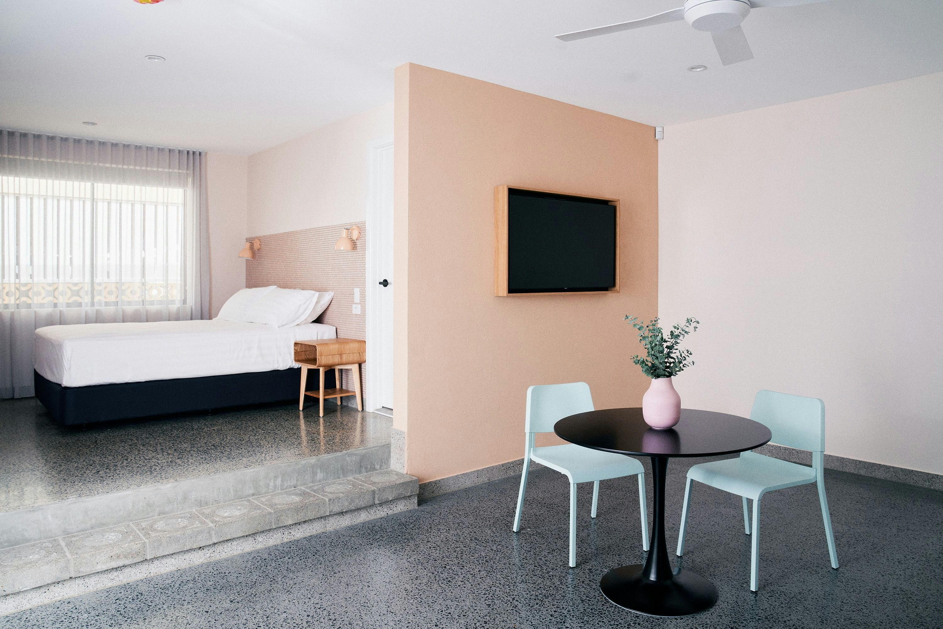 a motel room with a small table with turqoise chairs and a salmon pink wall and a tv
